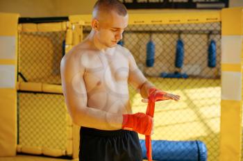 Male MMA fighter wraps bandages on his hands in gym. Muscular man on ring prepares for combat, martial arts training