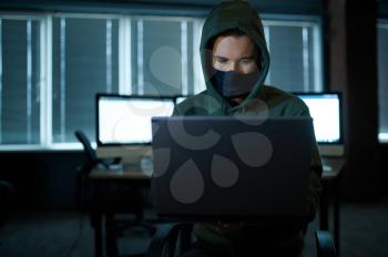 Male internet hacker in hood holds laptop, front view. Illegal web programmer at workplace, criminal occupation. Data hacking, cyber security