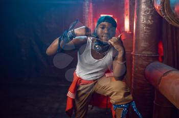 Stylish rapper shows his gold jewelry in studio with cool underground decoration. Hip-hop performer, rap singer, break-dance