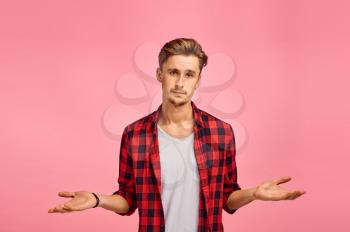 Serious man spreads his hands, pink background, emotion. Face expression, male person looking on camera in studio, emotional concept, feelings
