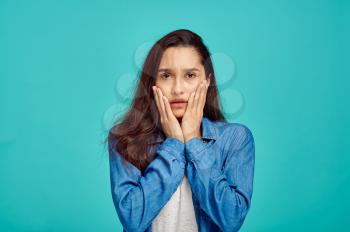 Young scared woman portrait, blue background, negative emotion. Face expression, female person looking on camera in studio, emotional concept, feelings