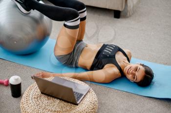 Girl doing exercise with ball, online pilates training at the laptop. Female person in sportswear, internet sport workout, room interior on background