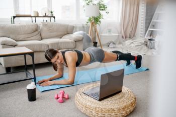 Smiling girl sits on the floor at home, online fit training at the laptop. Female person in sportswear, internet sport workout