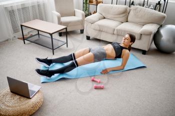 Woman doing abs exercise, online fitness training at the laptop. Female person in sportswear, internet sport workout, room interior on background