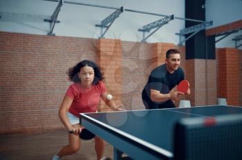 Man and woman play doubles table tennis, ping pong players. Couple playing table-tennis indoors, sport game with racket and ball, active healthy lifestyle