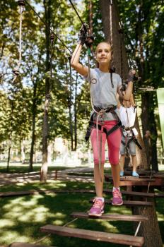 Little brother and sister climbs in rope park. Children climbing on suspension bridge, extreme sport adventure on vacations, entertainment outdoors