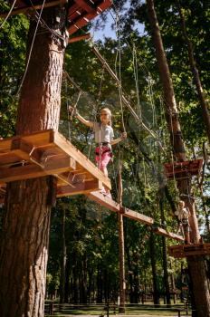 Little female climber leisures in rope park, playground. Child climbing on suspension bridge, extreme sport adventure on vacations, entertainment outdoors