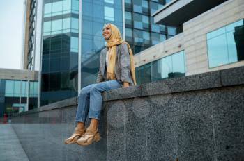 Arab girl in hijab poses at the building in downtown. Muslim woman at the entrance to the business center. Religion and education