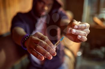 Drug addict man holds syringe with dose in hellhole, shebang interior on background, den. Narcotic addiction problem, eternal depression of junky people