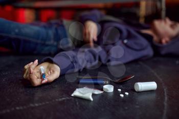 Drug addict man lying on the floor in den, shebang interior on background, overdose. Narcotic addiction problem, eternal depression of junky people