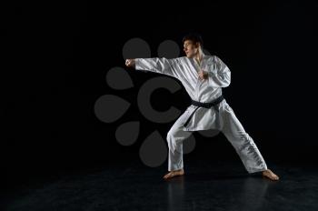 Male karate fighter in white kimono, combat stance, dark background. Man on karate workout, martial arts, fighting competition