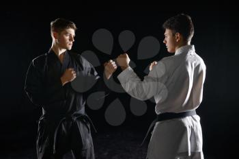 Two male karatekas in white and black kimono, strike, dark background. Fighters on workout, martial arts, fighting competition