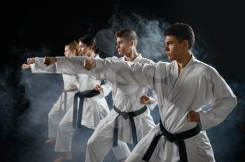 Four karate fighters poses in white kimono, group training, dark smoky background. Karatekas on workout, martial arts