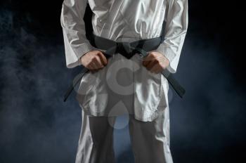 Male karateka, fighter having black belt, combat stance, dark background. Man on karate workout, martial arts, training before fighting competition