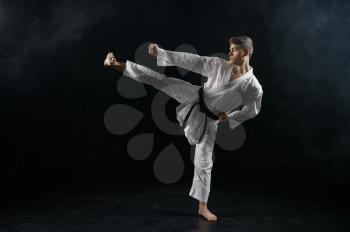 Male karateka, fighter in black kimono, combat stance, dark background. Man on workout, martial arts, training before fighting competition
