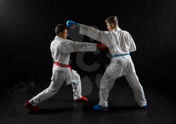 Two male karatekas in white kimono and gloves, strike in action, dark background. Fighters on workout, martial arts, fighting competition