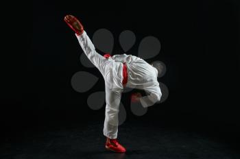Male karateka, fighter practice in white kimono and red gloves, combat stance, dark background. Man on karate workout, martial arts, training before fighting competition