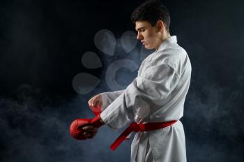 Male karate fighter in white kimono having red belt and gloves, combat stance, dark background. Karateka on workout, martial arts, training before fighting competition