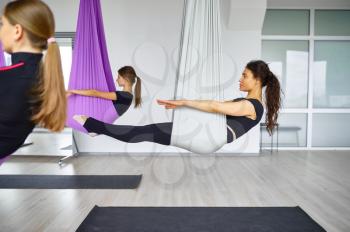 Aerial antigravity yoga, female group training, hanging on hammocks. Fitness, pilates and dance exercises mix. Women on yogi workout in sports studio
