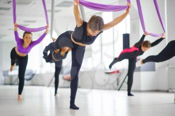 Aerial yoga studio, female group training, hanging on hammocks. Fitness, pilates and dance exercises mix. Women on yoga workout in gym