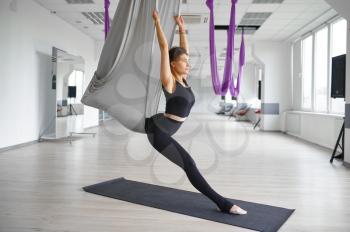 Aerial yoga, slim woman on hammock, stretching. Fitness, pilates and dance exercises mix. Female person on yogi workout in sports studio