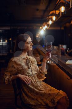 Alone young woman with glass of red wine sitting at the counter in bar. One female person in pub, human emotions, leisure activities, nightlife