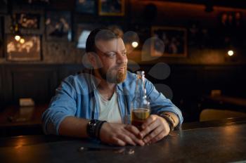 Cheerful man with bottle of beer sitting at the counter in bar. One male person in pub, human emotions, leisure activities, nightlife
