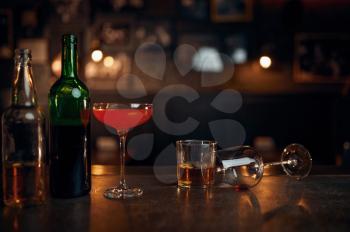 Different alcohol beverages on counter in bar, booze concept. Bottles and glasses on wooden table in pub closeup. Drinks assortment for stress relief or for fun