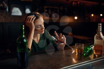 Unhappy woman drinks alcohol beverage at the counter in bar. One female person in pub, human emotions, leisure activities, depression