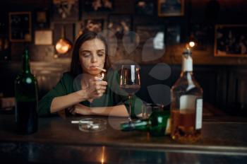Drunk woman smokes a cigarette at the counter in bar. One female person in pub, human emotions, leisure activities, depression
