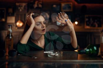 Depressed woman sitting at the counter in bar, full ashtray. One female person in pub, human emotions, leisure activities, depression