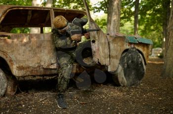 Paintball player in uniform and mask playing on playground in the forest. Extreme sport with pneumatic weapon and paint bullets or markers, military team game outdoors