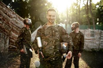 Paintball team, warriors poses on playground in the forest. Extreme sport with pneumatic weapon and paint bullets or markers, military game outdoors, combat tactics