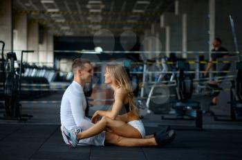 Sportive love couple sitting on the floor, training in gym. Athletic man and woman on workout in sport club, active healthy lifestyle, physical wellness