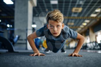 Boy doing push up exercise in gym, front view. Youngster on training in sport club, healthcare and healthy lifestyle, schoolboy on workout, sportive youth
