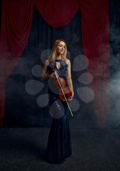 Female violonist holds bow and violin in retro style. Woman with string musical instrument, music art, musician play on viola, dark background