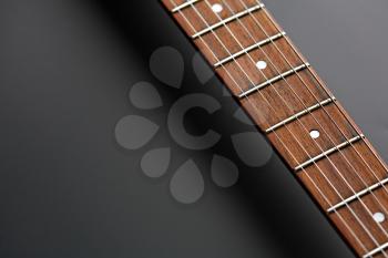 Electric guitar, closeup view on wooden fretboard, black background, nobody. String musical instrument, electro sound, electronic music, equipment for stage concert