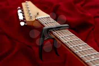 Electric guitar fretboard with capodaster, closeup, red background, nobody. String musical instrument, electro sound, electronic music, equipment for stage concert