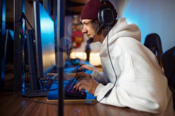 Young gamer in headset play shooter in game club. Virtual entertainment, e-sport tournament, cybersport lifestyle. Male person leisures in internet cafe