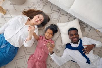 Happy family lying on the floor in living room. Mother, father and their daughter poses at home together, good relationship