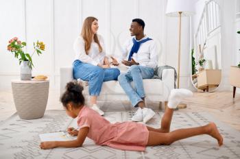 Happy family relaxing in living room. Mother, father and their little daughter poses at home together, good relationship. Mom, dad and female child, photo shoot in house