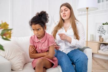 Mother scolds her little daughter on sofa in living room.Mom and sad female child, difficulties of raising children