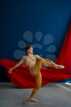 Male ballet dancer, balance exercise in dancing studio, blue walls and red cloth on background. Performer with muscular body, grace and elegance of movements
