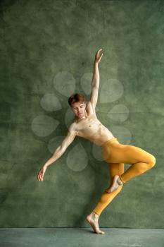 Male ballet dancer poses at grunge wall in dancing studio. Performer with muscular body, grace and elegance of movements
