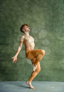 Male ballet dancer poses at grunge wall in dancing studio. Performer with muscular body, grace and elegance of dance