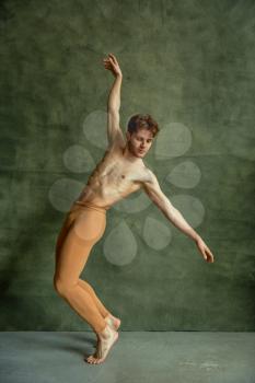 Male ballet dancer poses at grunge wall in dancing studio. Performer with muscular body, grace and elegance of dance