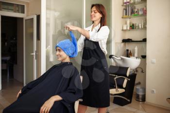 Hairdresser puts towel on woman's hair, front view, hairdressing salon. Stylist and client in hairsalon. Beauty business, professional service