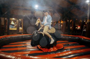 Young man on rodeo attraction in night amusement park. Family relax outdoors. Love couple leisures on carousels, entertainment theme