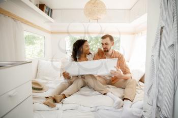 Love couple sitting in bed with map, camping in a trailer. Man and woman travels on van, romantic vacations on motorhome, campers leisures in camping-car