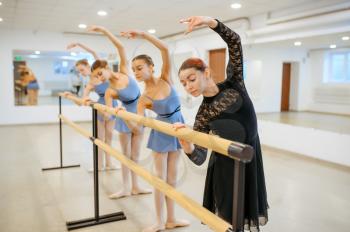 Master and young ballerinas rehearsing at the barre in class. Ballet school, female dancers on choreography lesson, girls practicing grace dance
